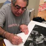 Jim Marshall signs his iconic Johnny Cash print for Brad Mangin in his San Francisco home on February 11, 2009. (Photo by Grover Sanschagrin)
